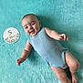 baby, infant, smiling, lying_down, blue_clothing, onesie, blanket, turquoise, face, happy, cute, child, skin, arm, leg, foot, sign, flower, text, portrait
