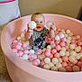 Walker is registered to the contest to win money with this photo: baby, ball_pit, pink, white, translucent, balls, child, smiling, indoor, carpet, happy, toddler, play, toy, person, sitting, holding, short_hair, grey_shirt, nike