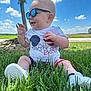 Walker is registered to the contest to win money with this photo: baby, sunglasses, grass, outdoor, blue_sky, clouds, tree, field, smiling, child, summer, sunny, toddler, white_shoes, shorts, shirt, patriotic, happy, nature, casual