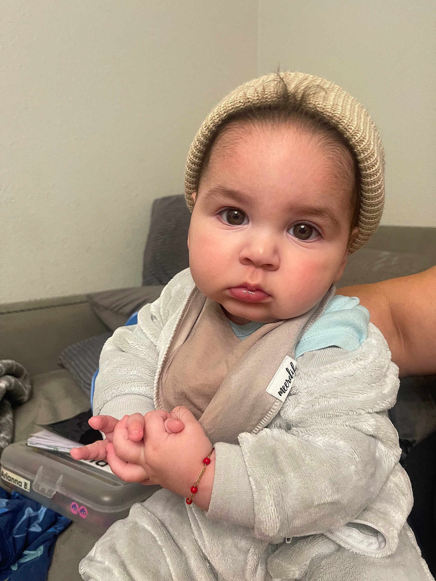 Ezra is registered to the contest to win money with this photo: baby, child, indoor, hat, beanie, clothing, hands, face, expression, person, cute, portrait, warm, soft, jacket, couch, bracelet, skin, eyes, sitting