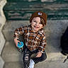 child, boy, smiling, beanie, plaid_shirt, sippy_cup, steps, concrete, casual_clothing, white_sneakers, ripped_jeans, outdoor, portrait, happy, young, person, seated, blue_lid, brown_hat, cute