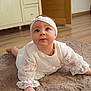 baby, infant, child, white_dress, headband, blue_eyes, curious, lying_down, rug, wooden_floor, indoor, furniture, cabinet, soft_lighting, crawling, cute, portrait, person, home, decor