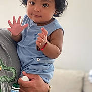 Denilson is registered to the contest to win money with this photo: toddler, child, hat, blue_clothing, curly_hair, person, hand, tattoo, bottle, adult, indoor, couch, footwear, sandals, bracelet, smiling, holding, portrait, casual, cute
