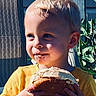 baby, birthday, blue_background, burger, child, close_up, food, frosting, hands, happy, messy_face, outdoor, plant, portrait, sandwich, smiling, sprinkles, sunlight, toddler, yellow_shirt