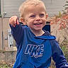 Hudson is registered to the contest to win money with this photo: child, boy, toddler, smiling, happy, portrait, outdoor, hoodie, blue_clothing, pointing, face, blond_hair, teeth, standing, garden, house, plants, daylight, casual, photography