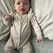 Cambree is registered to the contest to win money with this photo: baby, infant, onesie, sleepwear, bed, pillow, blanket, lying_down, cute, tongue_out, child, person, soft_lighting, indoors, expression, cozy, pastel_colors, socks, textile, sleeping_area