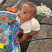 Zyaire joined the competition — help win amazing prizes! baby, child, infant, onesie, curly_hair, carpet, play_mat, colorful, indoor, toy, crawling, cute, floor, patterned, expression, skin, hand, face, person, curious