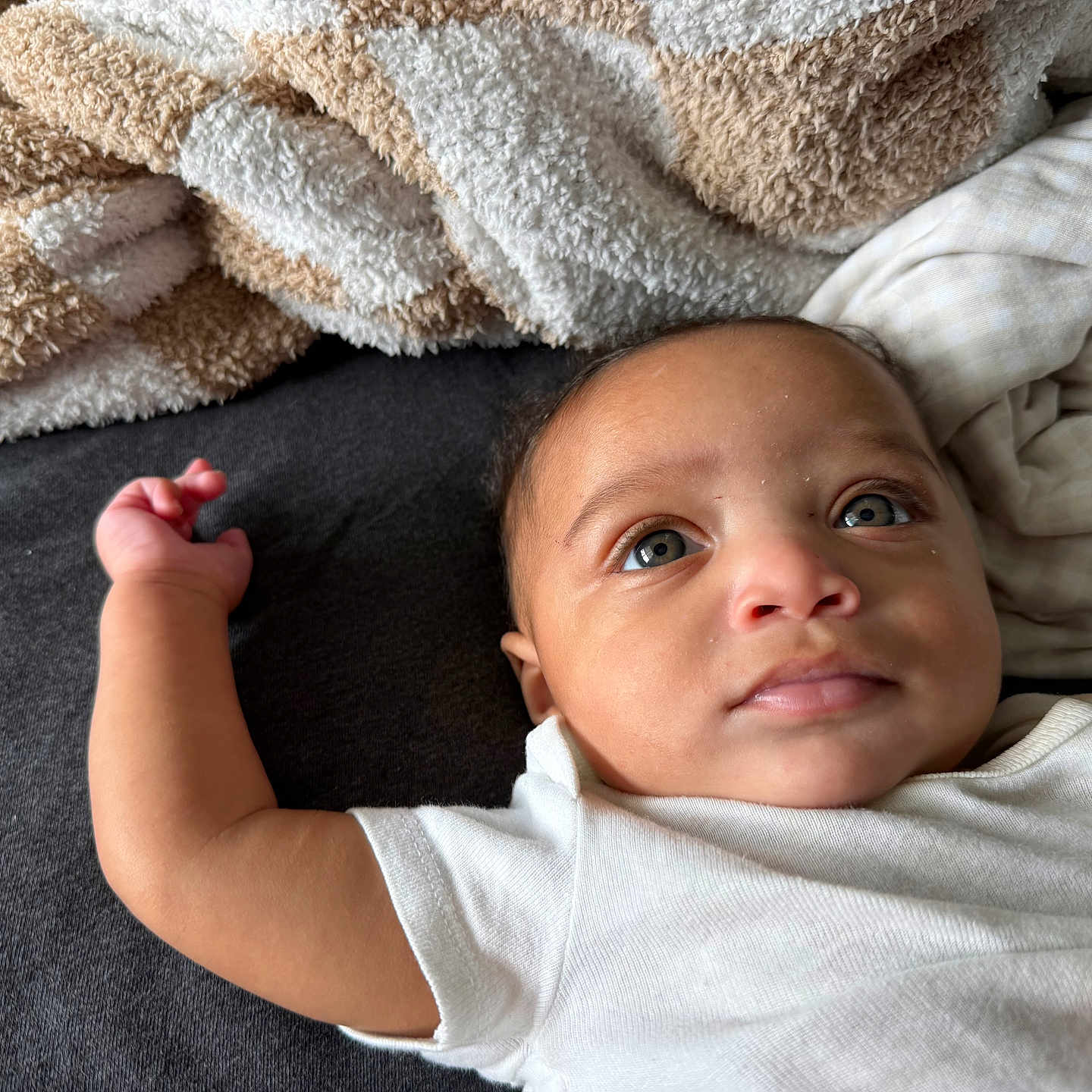 Zyaire joined the competition — help win amazing prizes! baby, infant, child, face, eyes, skin, blanket, fabric, texture, clothing, white_shirt, lying_down, portrait, indoor, soft_light, cute, expression, arm, hand, closeup