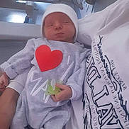 Maxence a rejoint le concours — aidez-le/la à gagner de superbes lots ! baby, newborn, infant, hospital_bed, onesie, heart_shape, pacifier, beanie, parent_arm, sleeping, blanket, hospital, medical_equipment, tshirt, lying_down, closeup, cute, portrait, hand, skin