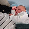 baby, black_jacket, closeup, cuddled, cute, green_pants, human, indoors, infant, newborn, peaceful, person, portrait, relaxed, resting, sleeping, soft_lighting, striped_shirt, toddler, white_clothing