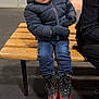 Ismaël a rejoint le concours — aidez-le/la à gagner de superbes lots ! child, toddler, wooden_bench, puffer_jacket, gloves, ice_skates, skates, jeans, curly_hair, smiling, sitting, indoor_rink, boots, laces, person, floor, background_chairs, jacket_hood, metal_blades, winter_clothing