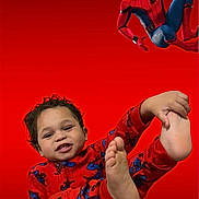 Ismaël participe au concours pour gagner de l'argent avec cette photo : child, toddler, pajamas, spiderman, superhero, red_background, smile, foot, feet, playful, costume, masked_character, comic_character, portrait, pose, indoor, patterned_clothing, camera_looking, young_child, bright_color