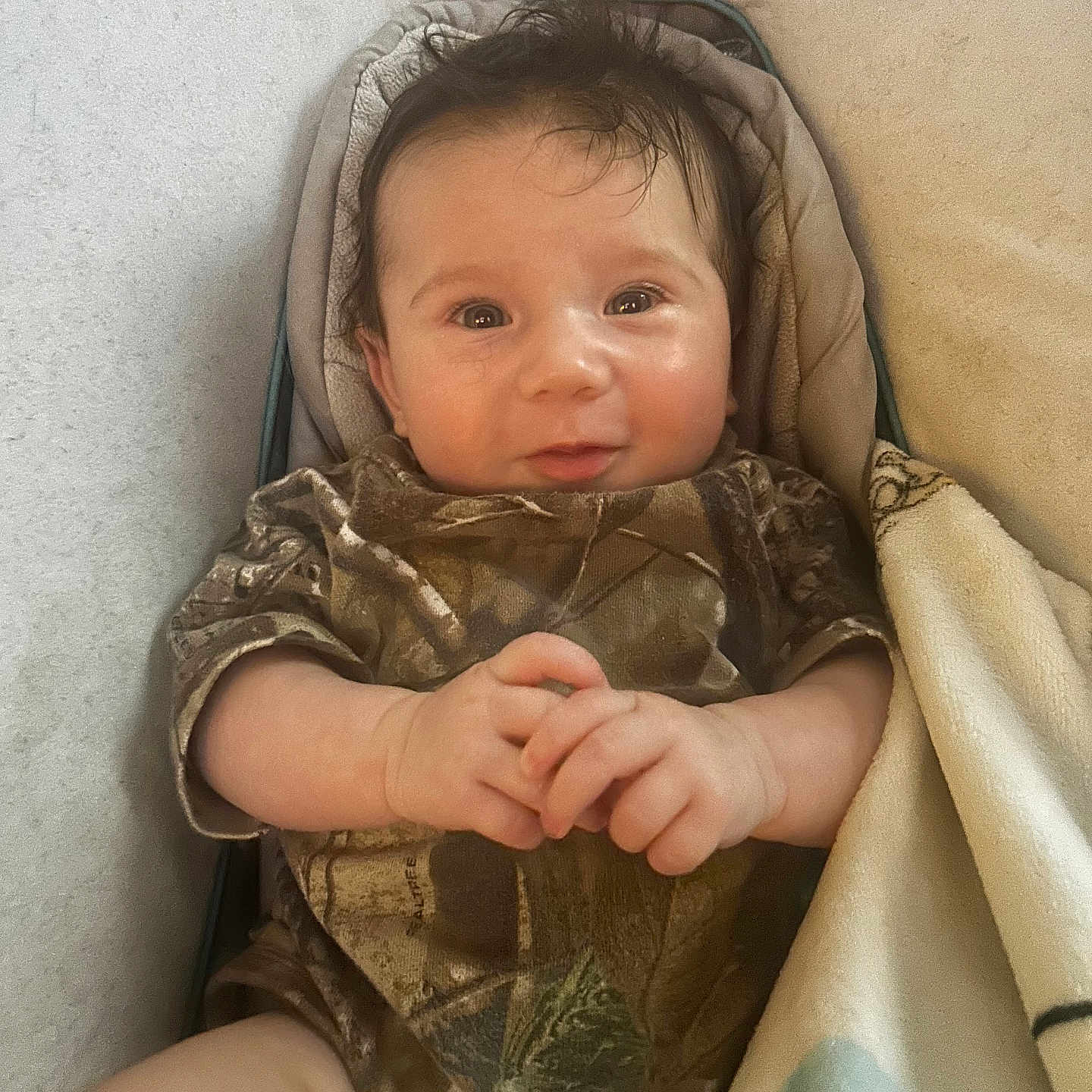 Grayson joined the competition — help win amazing prizes! baby, infant, smiling, camo_clothing, blanket, lying_down, cute, hand_gesture, indoors, portrait, child, young, cozy, soft_lighting, face, small_hands, happy, person, resting, warm