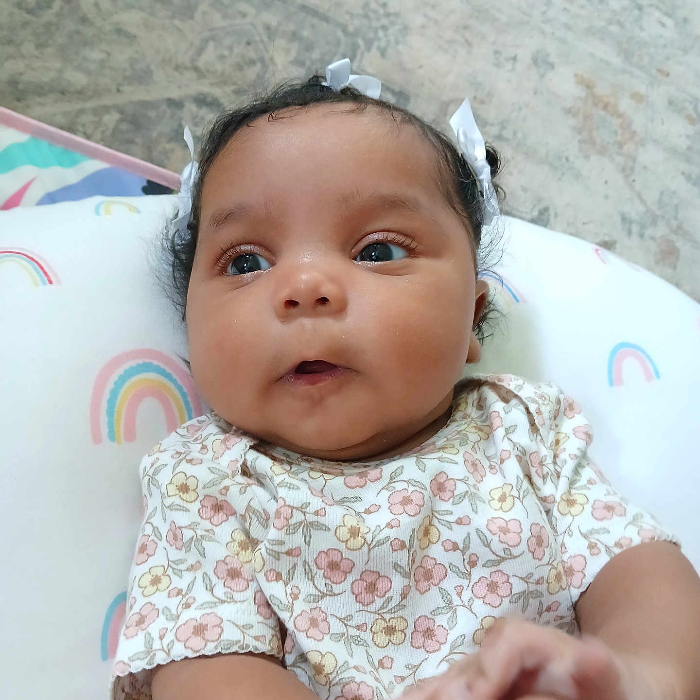 Sophia is registered to the contest to win money with this photo: baby, bows, child, closeup, curly_hair, cushion, cute, expression, eyes, face, floral_clothing, hair, hands, indoor, infant, laying_down, person, portrait, rainbow_pattern, skin