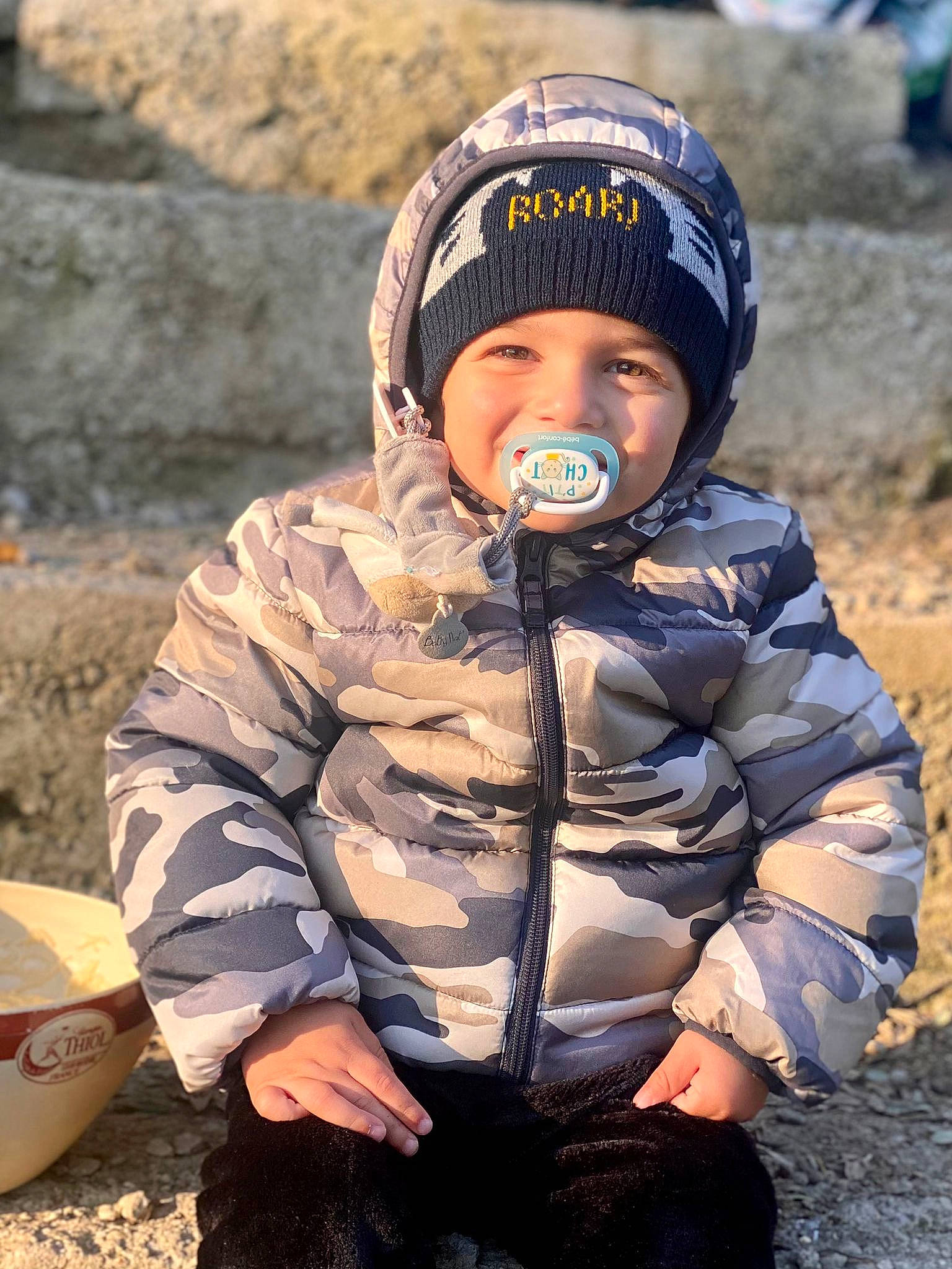 Gabriel a rejoint le concours — aidez-le/la à gagner de superbes lots ! camouflage, cap, child, eye, fun, glove, grass, headwear, jacket, joy, landscape, military_camouflage, outerwear, pattern, people_in_nature, person, personal_protective_equipment, sand, sitting, sleeve