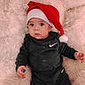 baby, infant, santa_hat, black_clothing, nike_logo, blanket, fur_texture, portrait, cute, holiday, christmas, indoors, child, young, smiling, face, hand, sitting, cozy, soft