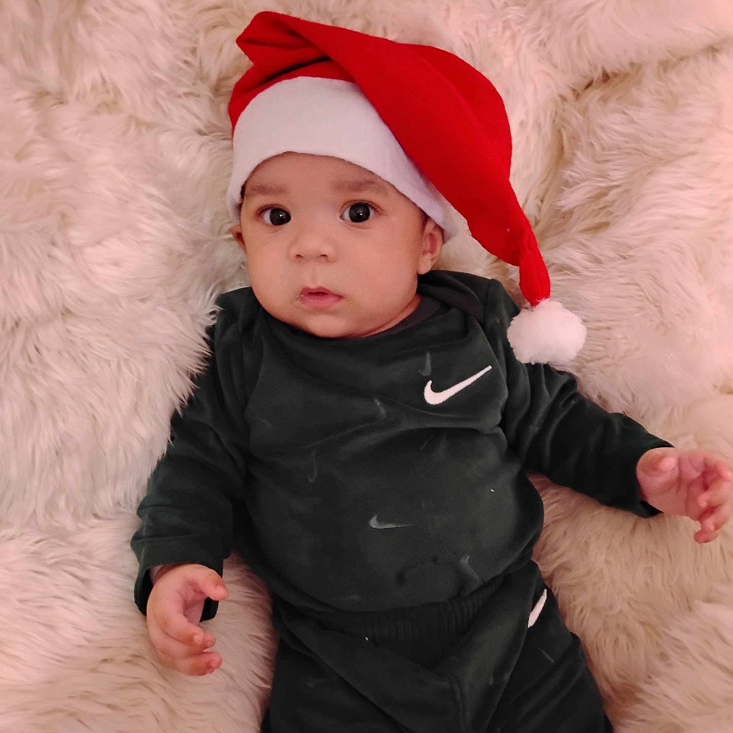 Jamari joined the competition — help win amazing prizes! baby, infant, santa_hat, black_clothing, nike_logo, blanket, fur_texture, portrait, cute, holiday, christmas, indoors, child, young, smiling, face, hand, sitting, cozy, soft