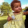 child, toddler, baby, girl, curly_hair, dress, yellow_dress, daisies, flower_pattern, earring, outdoor, park, grass, trees, blue_sky, clouds, being_held, portrait, looking_away, sunlight