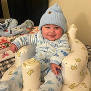 Jordan joined the competition — help win amazing prizes! child, baby, infant, smiling, blue_beanie, hat, onesie, plush_chair, inflatable_seat, blanket, bedding, pillow, indoors, cozy, rosy_cheeks, adorable, sitting, hand, face, portrait