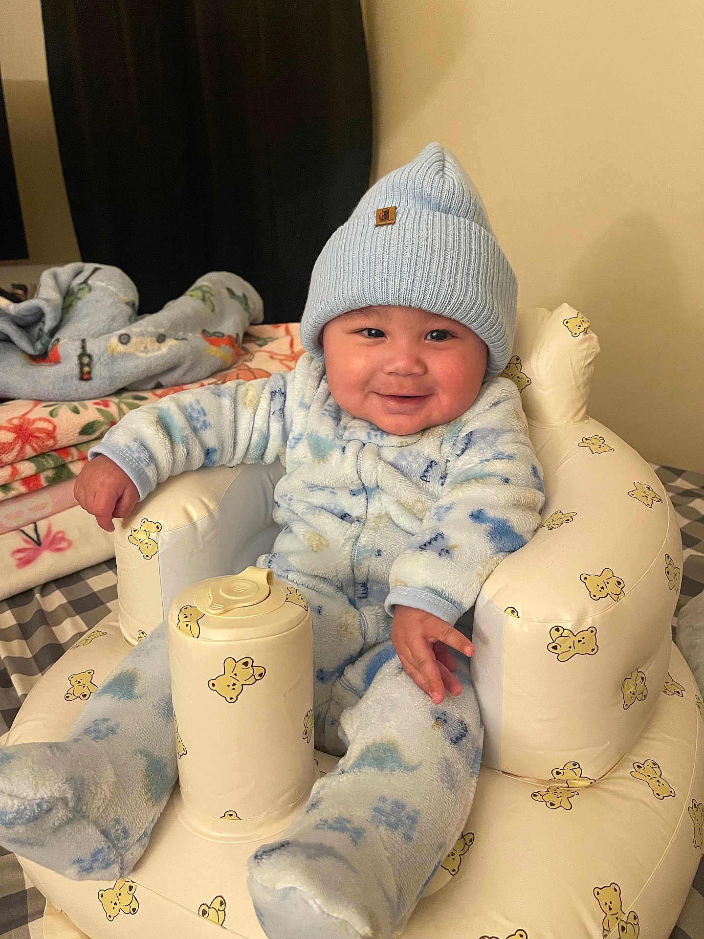 Jordan joined the competition — help win amazing prizes! child, baby, infant, smiling, blue_beanie, hat, onesie, plush_chair, inflatable_seat, blanket, bedding, pillow, indoors, cozy, rosy_cheeks, adorable, sitting, hand, face, portrait