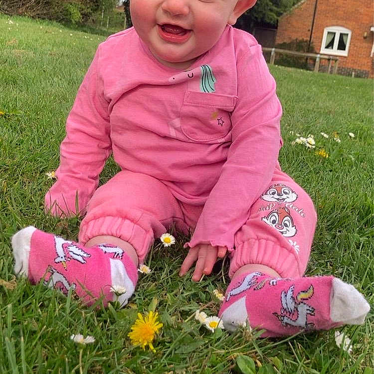 Elsie is registered to the contest to win money with this photo: baby, casual, child, cute, daylight, flowers, grass, greenery, happy, house, nature, outdoor, pink_clothing, playful, sitting, smiling, socks, sunny_day, trees, young_child