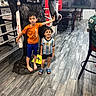 american_flag, blue_shorts, boys, chairs, child, children, football, furniture, gorilla_statue, high_five, indoor, orange_shirt, playful, portrait, posing, restaurant, smiling, soccer_jersey, standing, wood_floor