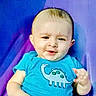 baby, blue_clothing, casual_clothing, child, close_up, colorful_background, elephant_shirt, eyes, face, happy, infant, joyful, mouth, outdoor, person, portrait, purple_background, short_hair, sitting, smiling