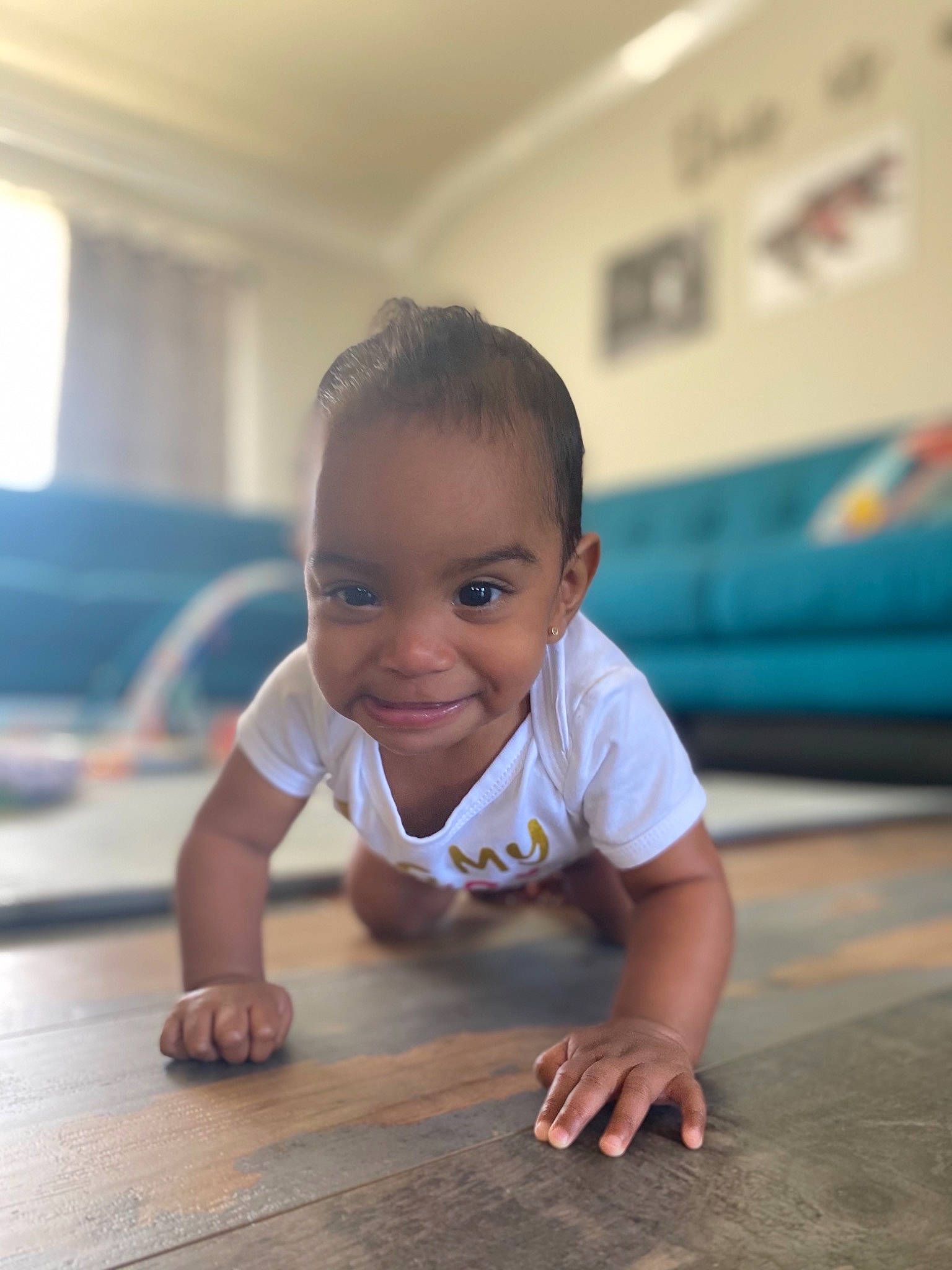 Aila is registered to the contest to win money with this photo: arm, baby, baby_toddler_clothing, cheek, chin, crawling, finger, floor, flooring, hairstyle, hand, happy, hardwood, joy, mouth, nose, person, skin, smile, standing