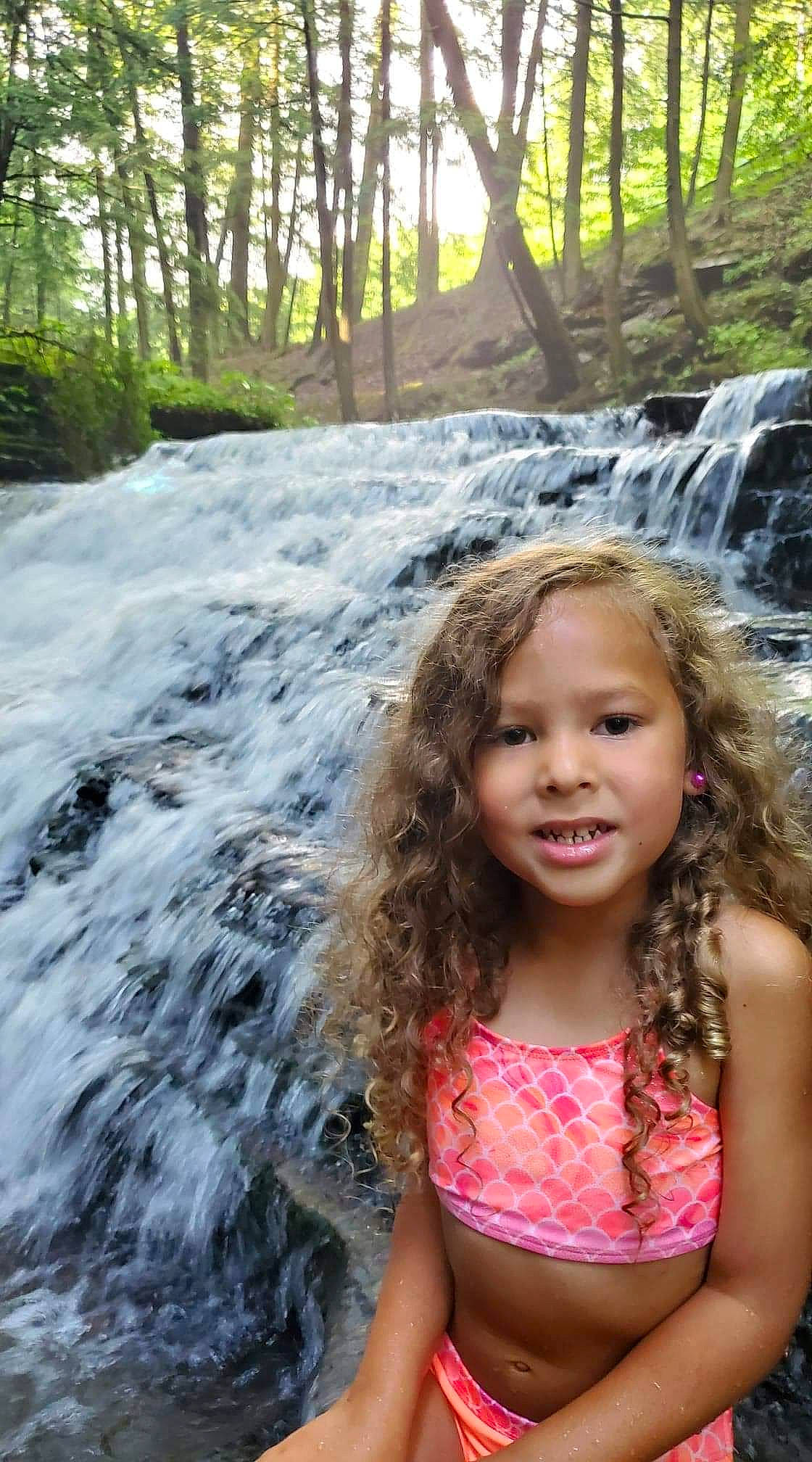 Kimora joined the competition — help win amazing prizes! body_of_water, eye, fun, grass, happy, head, leisure, long_hair, natural_landscape, people_in_nature, person, plant, recreation, summer, sunlight, toddler, tree, trunk, water, waterfall