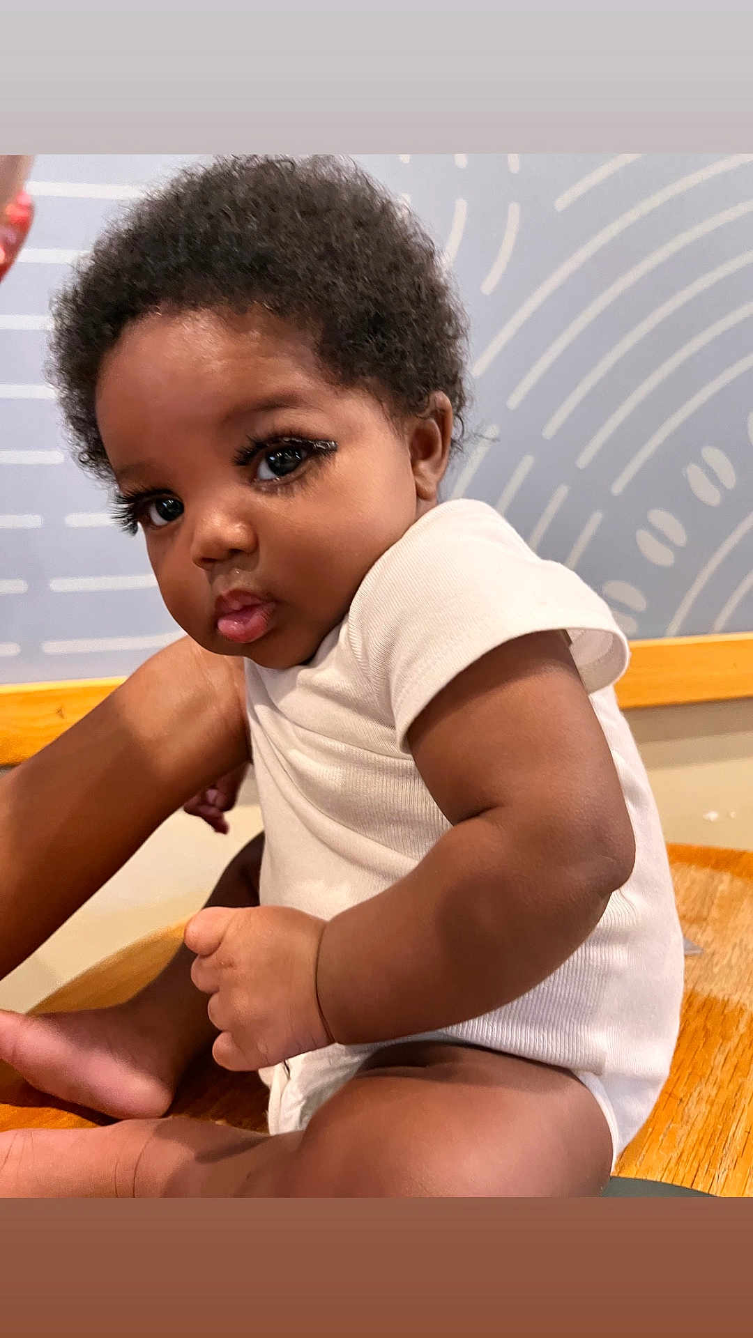 Chess is registered to the contest to win money with this photo: arm, baby, child, closeup, curly_hair, cute, expression, face, human, indoor, infant, leg, person, portrait, pout, sitting, skin, white_clothing, wooden_surface, young_child