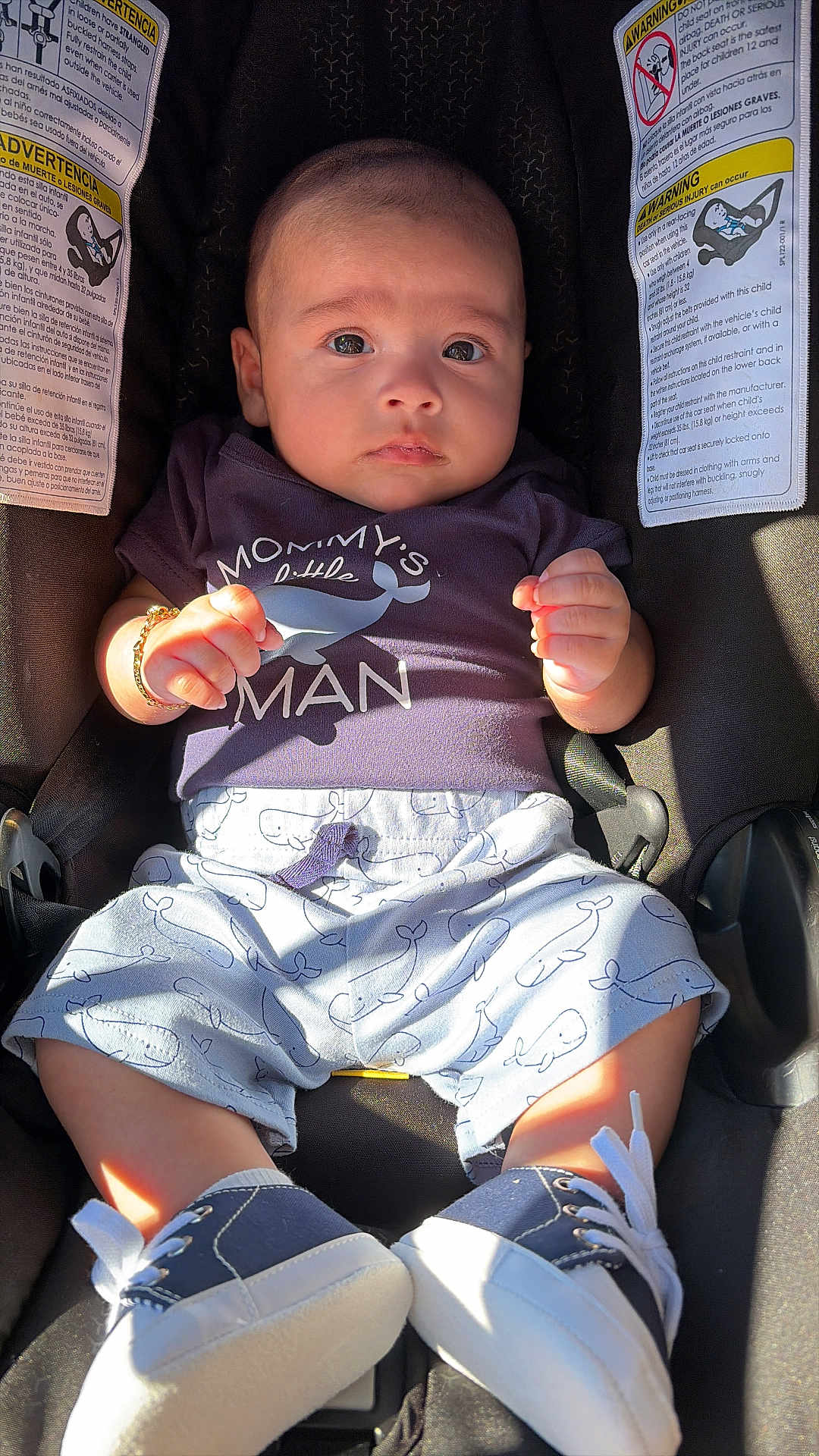 Noah is registered to the contest to win money with this photo: baby, infant, child, car_seat, onesie, baby_shoes, bracelet, face, eyes, hands, legs, sunlight, shadow, portrait, clothing, whale_pattern, safety_warning_label, carseat_harness, fabric, closeup