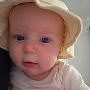 Lydia joined the competition — help win amazing prizes! baby, infant, face, eyes, hat, clothing, skin, head, portrait, indoor, cute, young_child, closeup, person, child, soft_lighting, curious, pink, yellow, expression