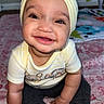baby, child, smiling, headband, yellow_bow, sitting, indoors, blanket, pink, pattern, cute, happy, person, clothing, infant, face, hands, feet, playmat, floor