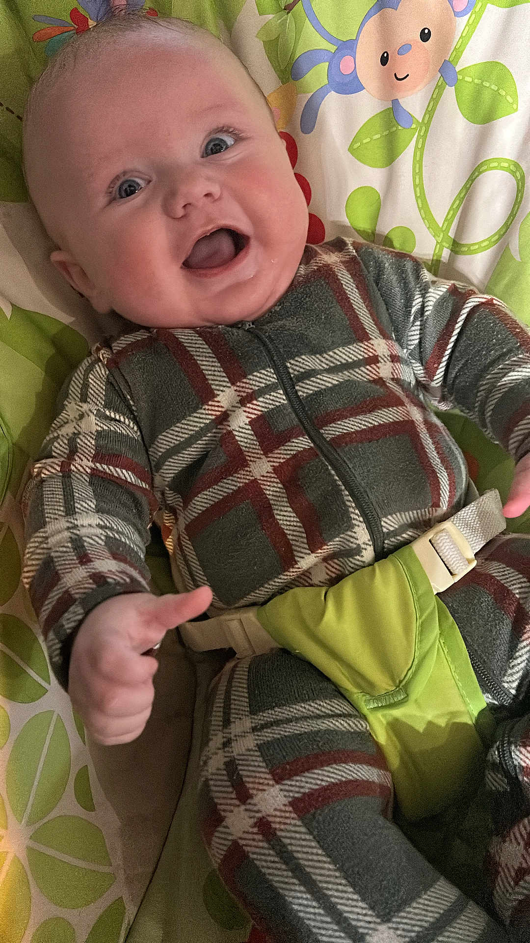 Rhett is registered to the contest to win money with this photo: baby, infant, smiling, plaid_clothing, onesie, baby_seat, child, happy, face, blue_eyes, playful, monkey_pattern, green, leaf_pattern, fabric, cute, indoor, person, seatbelt, young_child