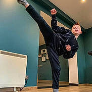 Hugo a rejoint le concours — aidez-le/la à gagner de superbes lots ! action, black_clothing, boy, child, furniture, hairstyle, heater, home, indoor, kick, martial_arts, modern_decor, mohawk, person, pose, practice, striped_socks, teal_wall, wooden_floor, young