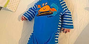Killian a rejoint le concours — aidez-le/la à gagner de superbes lots ! apparel, baby, blue_onesie, child, crab_design, curious_gaze, cute, fine_hair, indoors, infant, lying_down, newborn, person, plush_surface, resting, sleepwear, small_feet, small_hands, soft_lighting, white_bedding