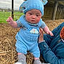 baby, blue_knitted_outfit, boots, bunny_ears, child, cute, daylight, farm, grass, hat, holding, infant, knitwear, nature, outdoor, person, playful, portrait, rosy_cheeks, straw