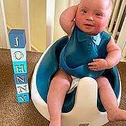 Killian participe au concours pour gagner de l'argent avec cette photo : arm_up, baby, baby_seat, bib, blocks, blue, carpet, child, curly_hair, diaper, face, floor, home, indoor, letters, person, railing, sitting, smiling, white