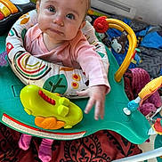 Gracey joined the competition — help win amazing prizes! baby, child, infant, headband, pink_clothing, activity_center, toys, blanket, indoor, cute, play, expression, face, person, small_hands, floor, colorful, seat, looking_up, curious