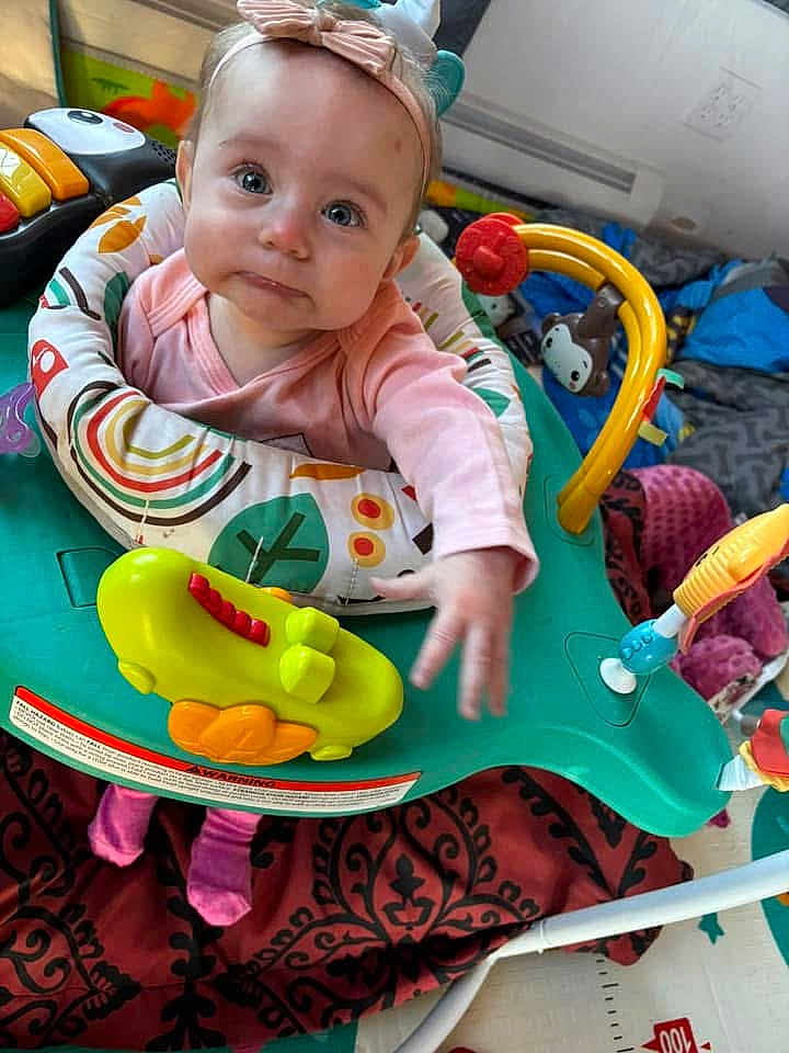 Gracey joined the competition — help win amazing prizes! baby, child, infant, headband, pink_clothing, activity_center, toys, blanket, indoor, cute, play, expression, face, person, small_hands, floor, colorful, seat, looking_up, curious