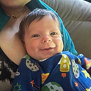 Damien is registered to the contest to win money with this photo: baby, smiling, child, person, adult, couch, clothing, necklace, indoor, portrait, face, happy, colorful, onesie, space_theme, furniture, closeup, skin, hair, light