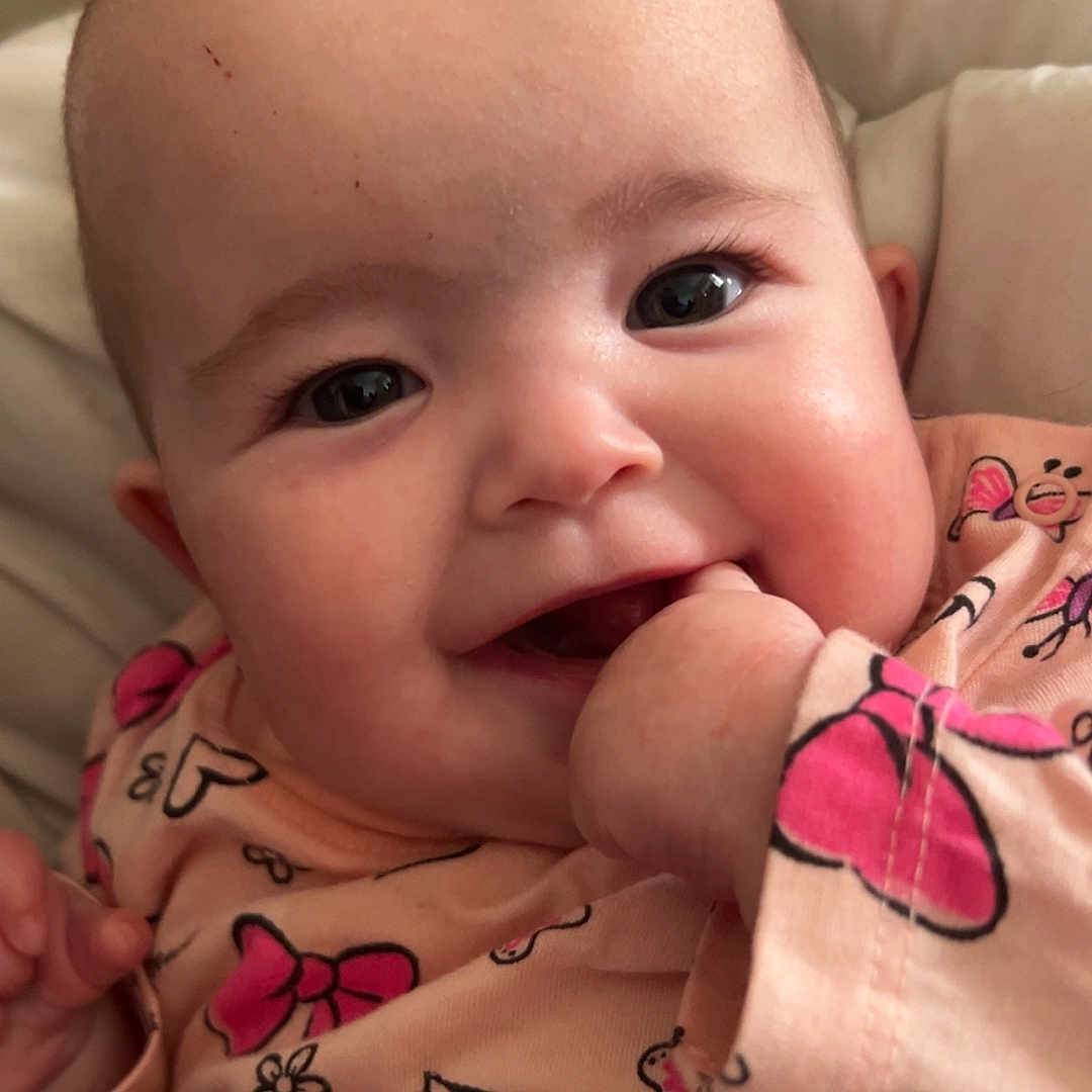 Ambre participe au concours pour gagner de l'argent avec cette photo : apparel, baby, bow_pattern, bright_eyes, butterfly_pattern, child, chubby_cheeks, close_up, cute, face, hand, happy, indoors, infant, person, pink_clothing, playful, sitting, smiling, soft_light