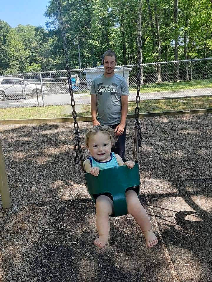 Jordon is registered to the contest to win money with this photo: baby, city, fun, grass, happy, joy, leisure, outdoor_play_equipment, person, plant, play, playground, recreation, shorts, sitting, sky, smile, soil, swing, t_shirt