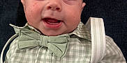 Parker is registered to the contest to win money with this photo: baby, infant, bow_tie, gingham_shirt, checked_shirt, smile, gummy_smile, face, eyes, cheeks, button, suspenders, closeup, portrait, seat, fabric, background, happy, cute, clothing