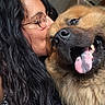 person, dog, kiss, happy, smile, tongue_out, glasses, long_hair, indoor, close_up, affection, animal, pet, casual_clothing, denim, black_hair, fluffy_dog, cute, companion, love