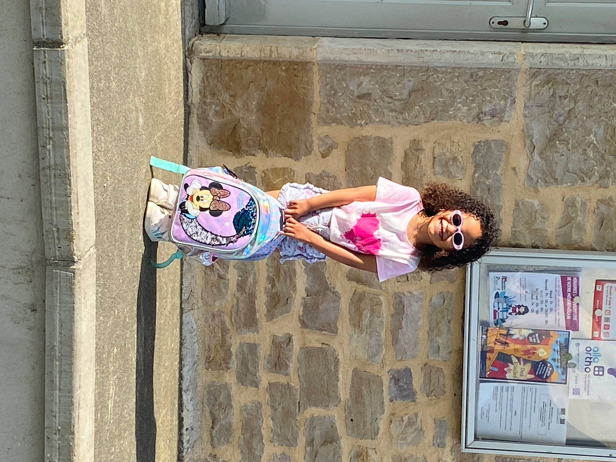 Divine a rejoint le concours — aidez-le/la à gagner de superbes lots ! advertising, art, child, eyewear, facade, human, human_leg, joy, leisure, line, pedestrian, person, pink, road, sidewalk, sitting, smile, street, street_art, travel