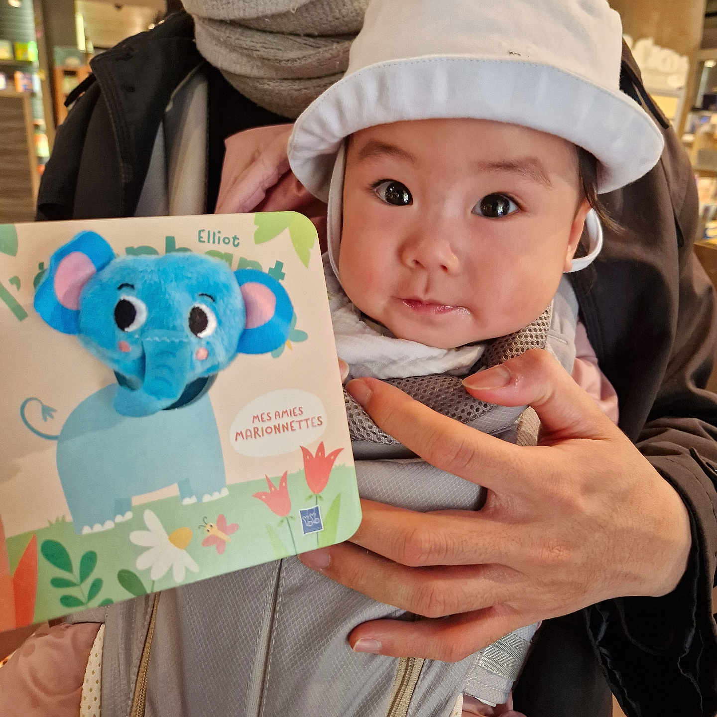 Mey participe au concours pour gagner de l'argent avec cette photo : adult, baby, background, book, carrier, child, clothing, curious, cute, elephant, face, hand, hat, holding, indoor, light, person, portrait, toy, wide_eyes