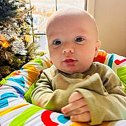 Walker is registered to the contest to win money with this photo: baby, infant, child, colorful, patterned_seat, christmas_tree, window, indoor, soft_lighting, cute, hands, sweater, holiday, decorations, portrait, young_child, face, seated, expression, home