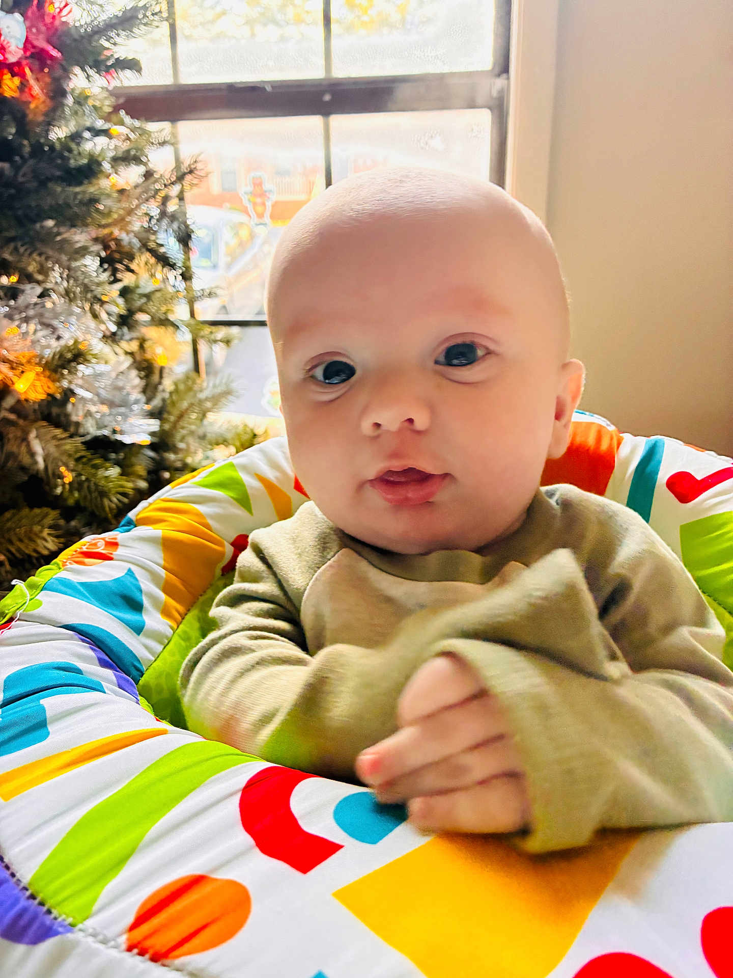 Walker is registered to the contest to win money with this photo: baby, infant, child, colorful, patterned_seat, christmas_tree, window, indoor, soft_lighting, cute, hands, sweater, holiday, decorations, portrait, young_child, face, seated, expression, home