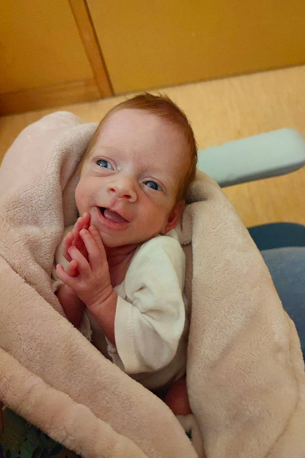 baby, blanket, clothing, cozy, cute, face, hands, happy, indoor, infant, newborn, person, portrait, skin, small, smiling, soft_texture, warm, wooden_floor, wrapped